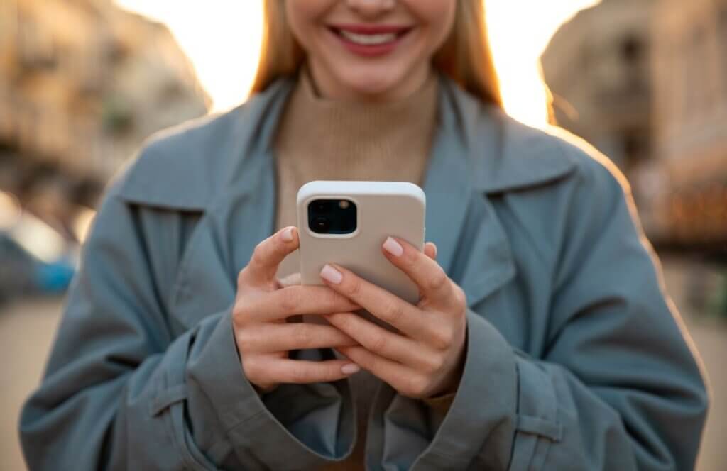 Woman holding a smartphone in city setting – modern technology containing small amounts of gold used in iPhone circuits and electronic components